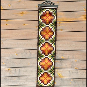 Könnte beinhalten: Ein Wandbehang mit einem sich wiederholenden Muster aus orangefarbenen, braunen und grünen Blumen. Der Wandbehang ist aus Stoff und wird mit einem schwarzen Metallhalter an der Wand befestigt.