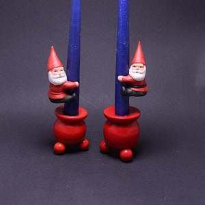Op de afbeelding: Twee blauwe kaarsen met rode houten kaarsenstandaards en kleine gnomenfiguren die op de kaarsen klimmen.