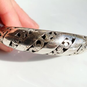 Puede incluir: Un brazalete plateado con un dise&ntilde;o calado. El brazalete presenta bandas entrelazadas con patrones arremolinados. El metal tiene un aspecto ligeramente envejecido. El dise&ntilde;o del brazalete recuerda a los nudos celtas.