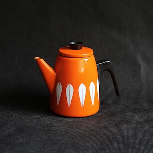 May include: An orange enamel teapot with a black handle and lid. The teapot features a white, teardrop-shaped pattern around the base. The spout is orange, and the lid has a black knob. A classic kitchenware item.