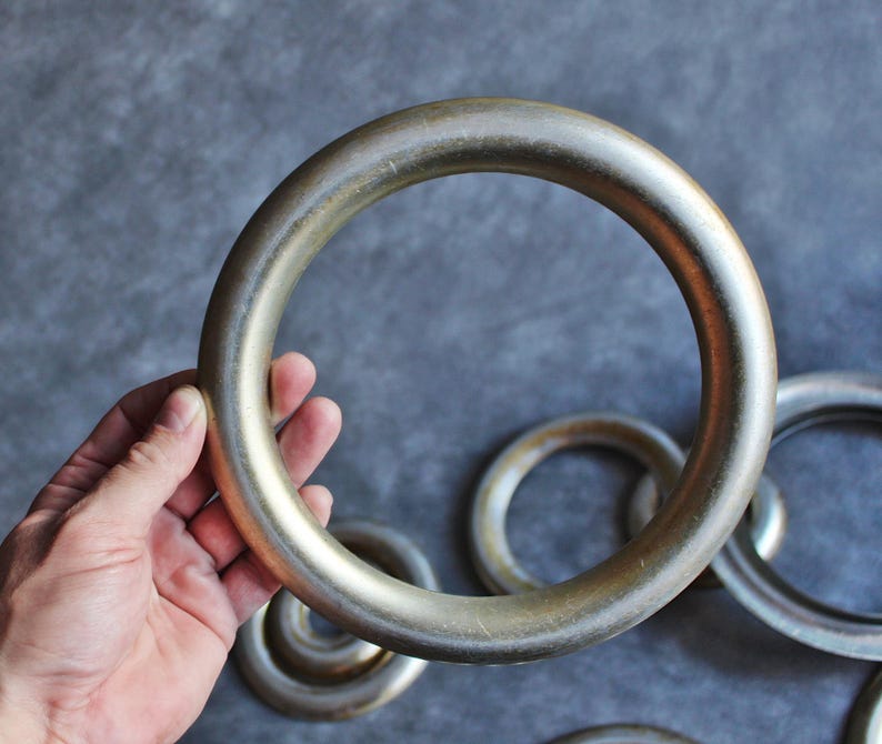 Puede incluir: Varios anillos met&aacute;licos grandes. Uno es sostenido por una mano, con otros de diferentes tama&ntilde;os en el fondo. Los anillos tienen una forma lisa y redondeada, con una apariencia ligeramente envejecida.