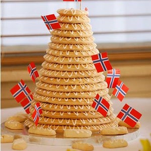 Puede incluir: Una torre de galletas de color marr&oacute;n dorado, decoradas con glaseado blanco, est&aacute; adornada con peque&ntilde;as banderas noruegas. Las galletas est&aacute;n dispuestas en forma c&oacute;nica, parecida a un postre festivo. Varias galletas est&aacute;n esparcidas en la base.