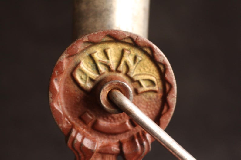 May include: Close-up of a vintage key with a circular, reddish-brown head. The head features the word "ANNA" in a gold-colored, stylized font. A silver-colored rod extends from the key head, suggesting a functional design. The key is likely for a lock.