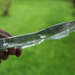 Puede incluir: Un plato de vidrio transparente con textura ondulada, sostenido por una mano sobre un fondo de hierba verde.