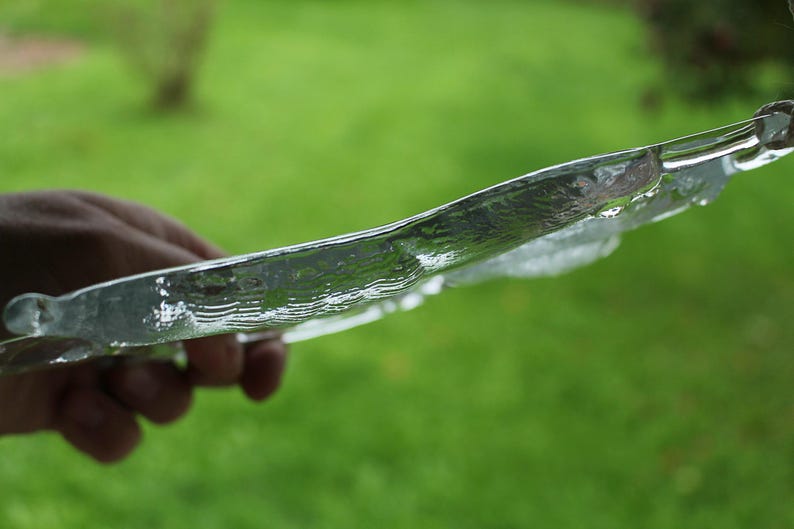 Puede incluir: Un plato de vidrio transparente con textura ondulada, sostenido por una mano sobre un fondo de hierba verde.