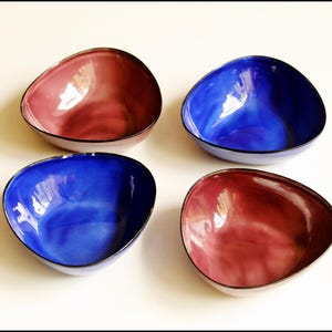 May include: Four ceramic bowls in a triangular shape. Two bowls are blue with a darker blue rim. Two bowls are a reddish-purple with a darker purple rim.