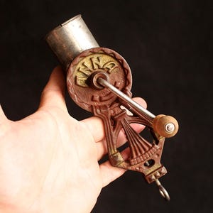May include: Antique hand-crank coffee grinder with a brown and gold finish. The grinder features a silver hopper and a wooden handle. The word "KING" is embossed on the grinder's wheel. A vintage kitchen tool.