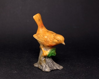 ビンテージ鳥の置物 ビンテージの素焼き磁器の鳥の置物。緑の葉と黄色い花の付いた枝の上で