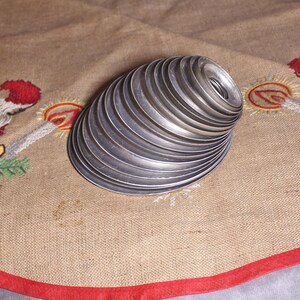 Puede incluir: Una pila de anillos de metal plateado, posiblemente para un proyecto de manualidades, dispuestos en forma de espiral. Los anillos est&aacute;n sobre una tela beige con un borde rojo y bordados navide&ntilde;os.