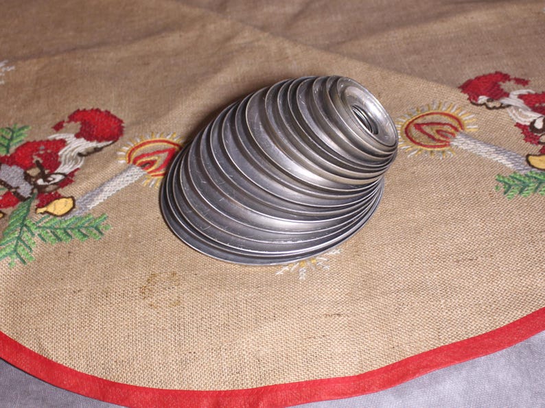 Puede incluir: Una pila de anillos de metal plateado, posiblemente para un proyecto de manualidades, dispuestos en forma de espiral. Los anillos est&aacute;n sobre una tela beige con un borde rojo y bordados navide&ntilde;os.