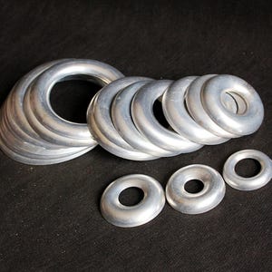 Puede incluir: Un conjunto de anillos met&aacute;licos plateados de varios tama&ntilde;os, dispuestos sobre una superficie negra. Los anillos tienen un dise&ntilde;o liso y redondeado, con un agujero en el centro. El conjunto de anillos m&aacute;s grande mide unos 10 cm de di&aacute;metro.