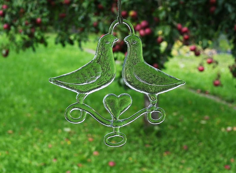 Puede incluir: Un carill&oacute;n de viento de vidrio con dos palomas y un encanto en forma de coraz&oacute;n en el centro. Las palomas son de vidrio transparente y el coraz&oacute;n es esmerilado.