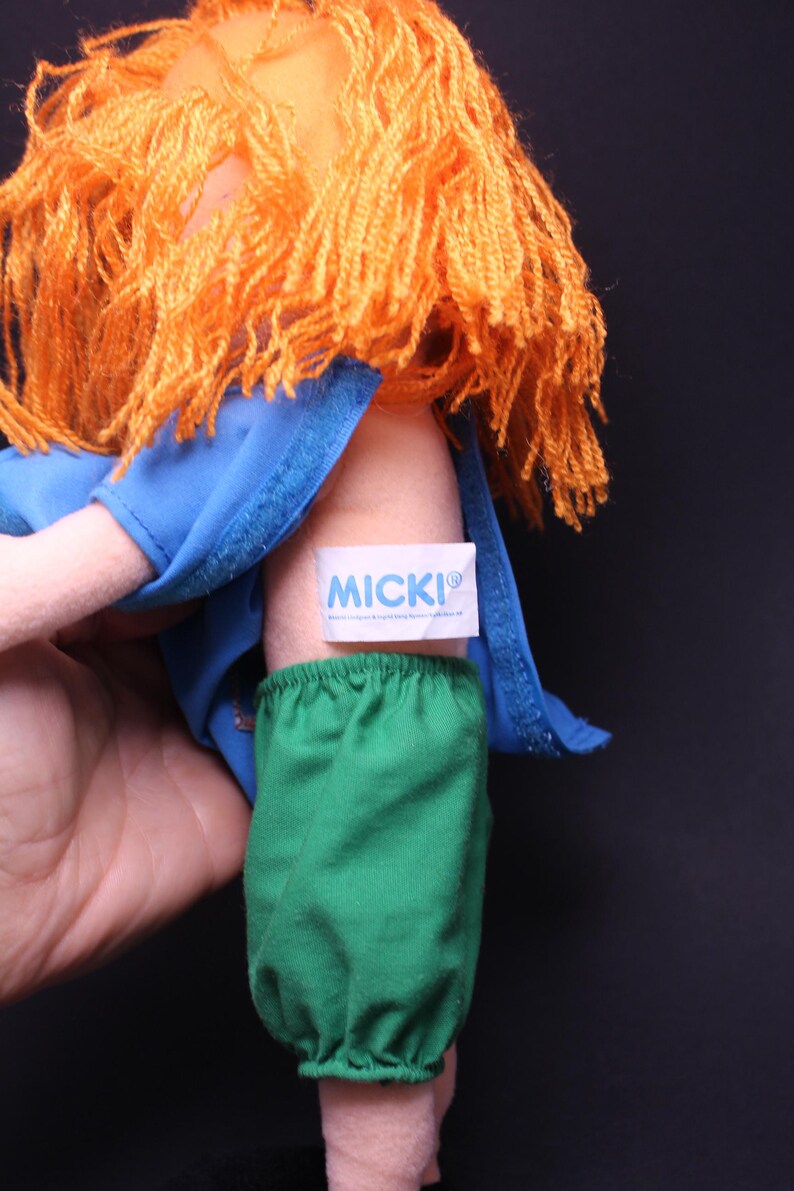 Pode incluir: Uma boneca vintage com cabelo de fio laranja, usando uma blusa azul e cal&ccedil;as verdes. A boneca tem uma etiqueta que diz "MICKI". Um brinquedo cl&aacute;ssico.