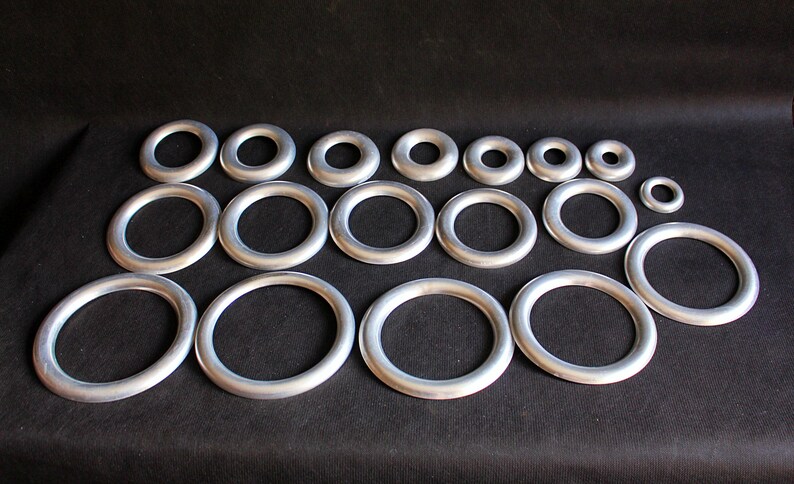 Puede incluir: Conjunto de anillos met&aacute;licos plateados de diferentes tama&ntilde;os, dispuestos sobre una superficie negra. Los anillos son circulares con un acabado liso y mate. Perfectos para manualidades y bisuter&iacute;a.