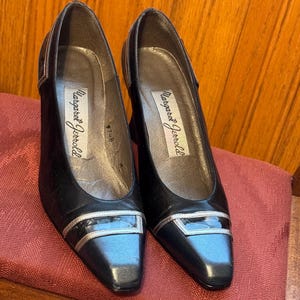 May include: A pair of black leather pumps with silver accents. The shoes have a pointed toe and a small heel. The brand name "Margaret Jerrold" is visible inside the shoe.