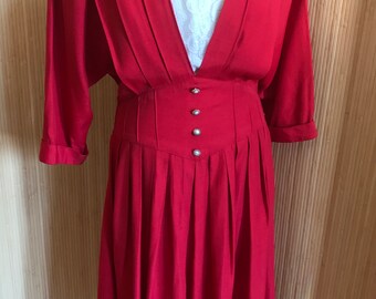 May include: A red dress with a V-neckline and a fitted bodice. The dress has a skirt with pleats and a button closure at the waist.