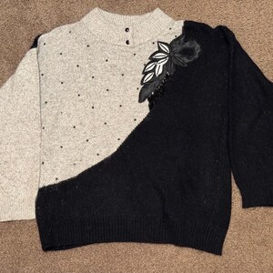 May include: A black and gray sweater with a floral design on the shoulder. The sweater has a high neck and long sleeves.