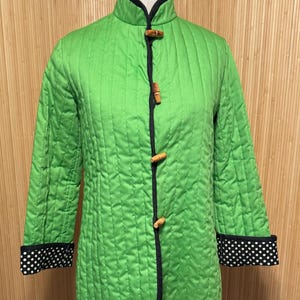 May include: A green quilted jacket with black trim and black and white polka dot cuffs. The jacket has wooden toggle closures.