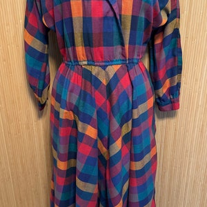 May include: A long-sleeved dress with a plaid pattern in shades of red, blue, green, and orange. The dress has a V-neckline and a gathered waist.