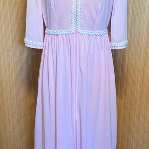 May include: A pink robe with a white trim around the neckline and sleeves. The robe has a zipper down the front and a gathered waist.