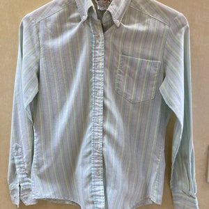 Puede incluir: Camisa abotonada con rayas verticales en colores pastel azul, rosa y amarillo. La camisa tiene un bolsillo en el pecho y mangas largas con puños abotonados. La marca "Licorice X" es visible en la etiqueta.