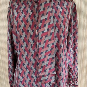 May include: A long-sleeved blouse with a geometric pattern in shades of red, brown, and white. The blouse has a tie at the neck.