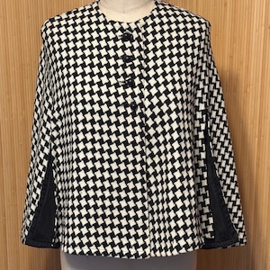 May include: Black and white checkered cape with black buttons and black trim on the sleeves.