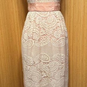 May include: A sleeveless, pink and white lace dress with a pink satin sash. The dress has a fitted bodice and a full skirt.