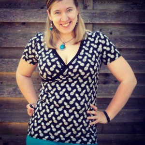 Könnte beinhalten: Eine Frau trägt ein schwarzes und weißes Wickeltop mit Ananas-Print und einer türkisfarbenen Halskette mit Anhänger.