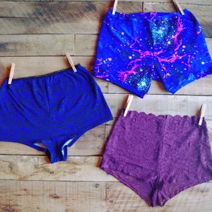 May include: Three pairs of women's shorts. One pair is blue with a galaxy print, one pair is blue with a black floral print, and one pair is purple with a lace pattern.