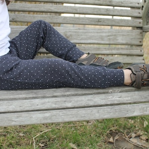 May include: Navy blue pants with a white polka dot pattern. The pants are cuffed at the ankles and are worn with brown and orange athletic shoes. A white t-shirt is also visible.