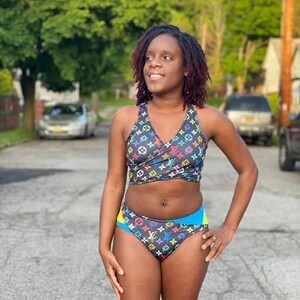 May include: A black and blue swimsuit with a colourful Louis Vuitton print. The top is a wrap style and the bottom is a high-cut bikini style.