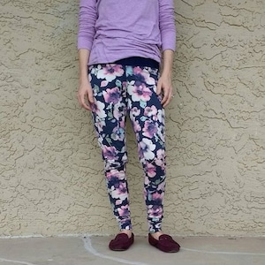 May include: A pair of dark blue leggings with a floral print in shades of pink, white, and purple. The leggings are fitted and have a cuffed hem.