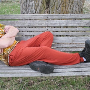 May include: A person wearing a tie-dye t-shirt and orange pants is resting on a wooden swing. The person is wearing black shoes. The swing is hanging from chains and is in a grassy area.