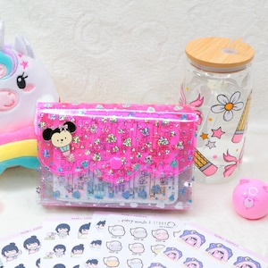 Puede incluir: Un unicornio de peluche blanco con vientre arcoíris, un estuche rosa con purpurina y un dije de Mickey Mouse, un vaso de vidrio transparente con tapa de bambú y dibujos de lápices, una varita rosa, una esfera rosa pequeña y hojas de pegatinas.