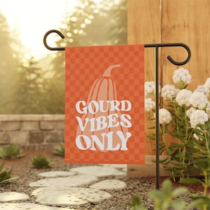 May include: A rectangular garden flag featuring an orange and light orange checkered pattern. A large, light-colored pumpkin illustration is centered on the flag, overlaid with the white text GOURD VIBES ONLY in a bold, wavy, retro-style font.