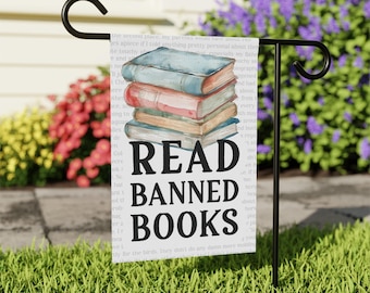 Puede incluir: Una bandera de jardín rectangular con una pila de cuatro libros de estilo acuarela en azul, rojo y beige. El texto READ BANNED BOOKS está impreso en letras mayúsculas negras grandes sobre un fondo de texto gris tenue y repetitivo.