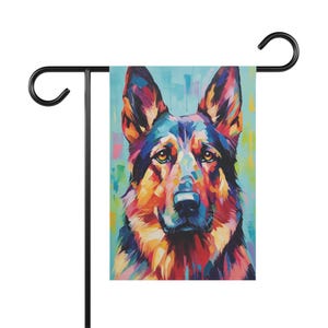 May include: A colorful garden flag featuring a vibrant, impressionistic portrait of a German Shepherd dog. The artwork uses a palette of blues, oranges, yellows, and reds. The flag is displayed on a black metal stand.