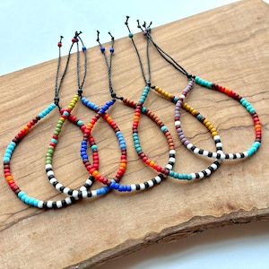 May include: Four adjustable bracelets made of small, multi-colored glass beads arranged in various patterns. Each bracelet features a black cord with sliding knots for closure, showcasing a vibrant mix of red, blue, turquoise, white, black, and yellow beads.