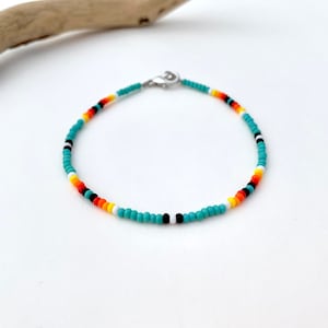 May include: A turquoise beaded bracelet with black, white, orange, and yellow beads. The bracelet is made with small, round beads and has a silver clasp.
