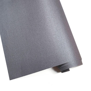 May include: A rolled sheet of gray, textured paper. The paper has a subtle sheen and a fine, woven-like pattern. The edges of the roll are visible, showing the layered construction of the material. The background is white.