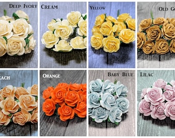 May include: Assortment of 10 paper roses in various colors, including deep ivory, cream, yellow, old gold, peach, orange, baby blue, and lilac. The roses are arranged in a circle on a wooden surface.