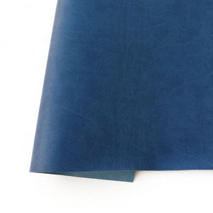 May include: A close-up of a folded piece of blue leather. The leather has a textured surface and a slightly faded appearance.