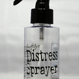 May include: A clear plastic bottle with a black spray nozzle and a black cap. The bottle is labeled "Distress Sprayer - for creating spray effects - Fill with water to use over Distress Ink, Paint, Stain & more Ranger".