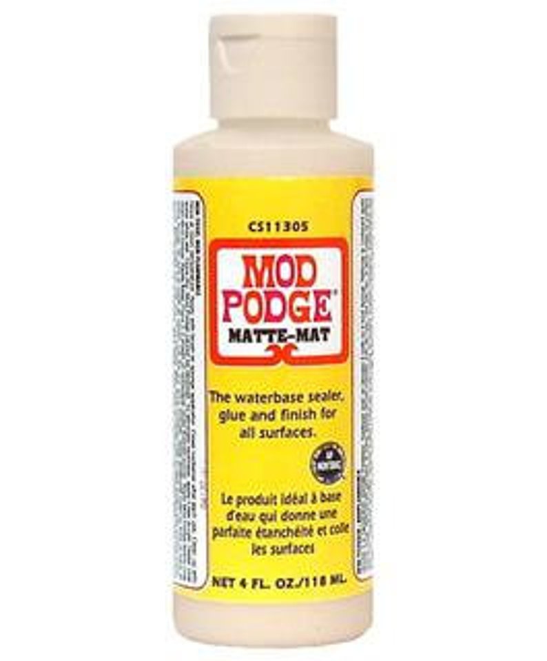 May include: A 4-ounce bottle of Mod Podge Matte-Mat water-based sealer, glue, and finish for all surfaces. The bottle is white with a yellow label and the text "CS11305 Mod Podge Matte-Mat" printed on it.