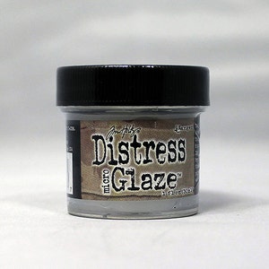 May include: A small gray jar of Distress Micro Glaze, a paint product by Tim Holtz. The jar has a black lid and a label that reads "Distress Glaze" with the word "micro" in smaller font above it. The label also includes the text "1 fl oz (30 ml)".