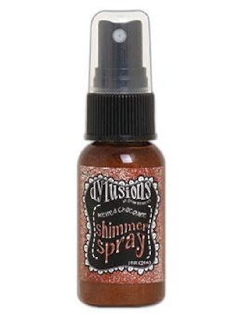 May include: A small bottle of Dylusions Shimmer Spray in the colour "Copper". The bottle is clear with a black spray nozzle and a black label with white text.