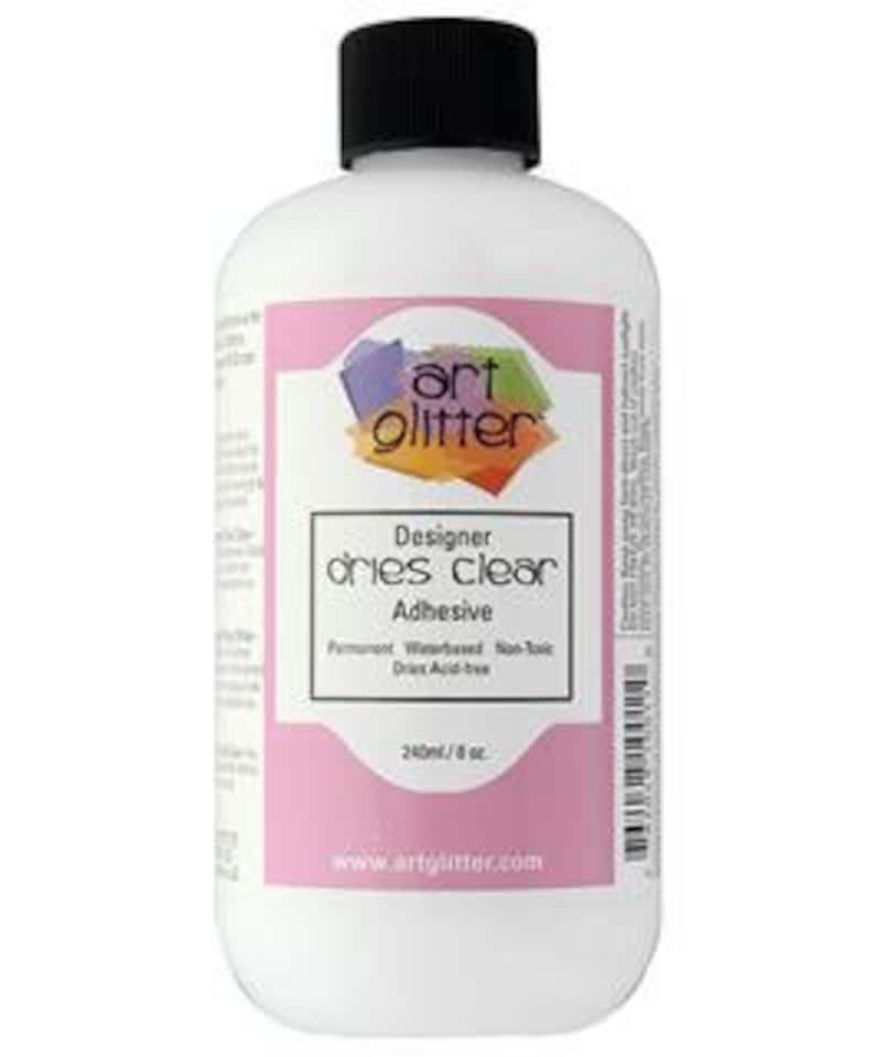 May include: A white bottle of Art Glitter Designer dries clear adhesive. The bottle is labeled with the brand name and product description. The bottle is 240 ml or 8 oz.