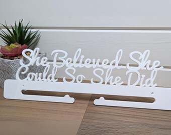 May include: White acrylic medal display with the text "She Believed She Could So She Did".