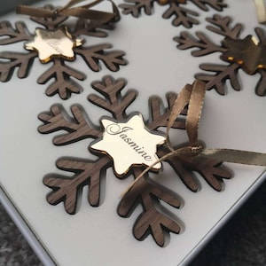 May include: A set of three wooden snowflake ornaments with gold star accents. Each snowflake has a personalised name on the star: "Willow", "Jasmine", and "Willow".